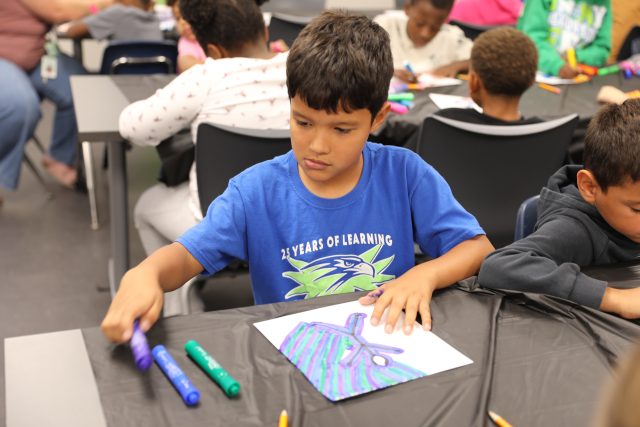 Photo caption: Third-graders at Meadow’s Edge Elementary experiment with line and pattern during an Art Smart lesson on color families. The PTO supplies program materials, and parent volunteers assist in the classroom.