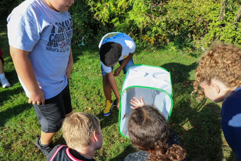 People gathered around a small white refrigerator in an outdoor setting.
