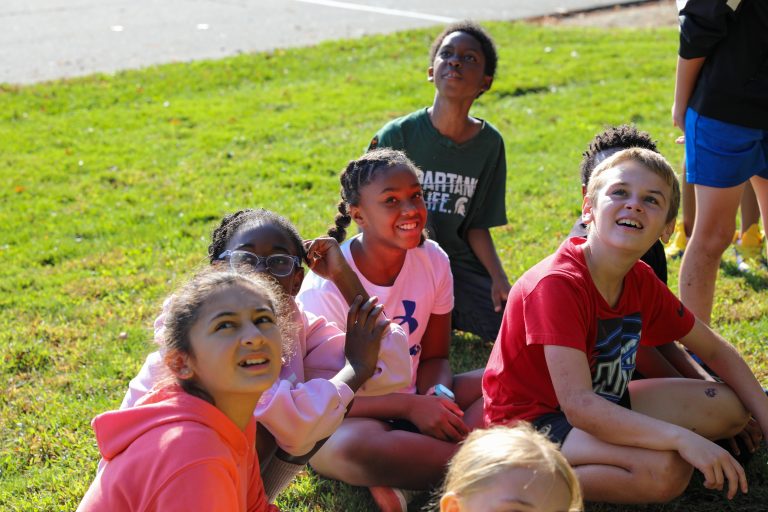 Group of children sitting on grass in park, smiling at camera.