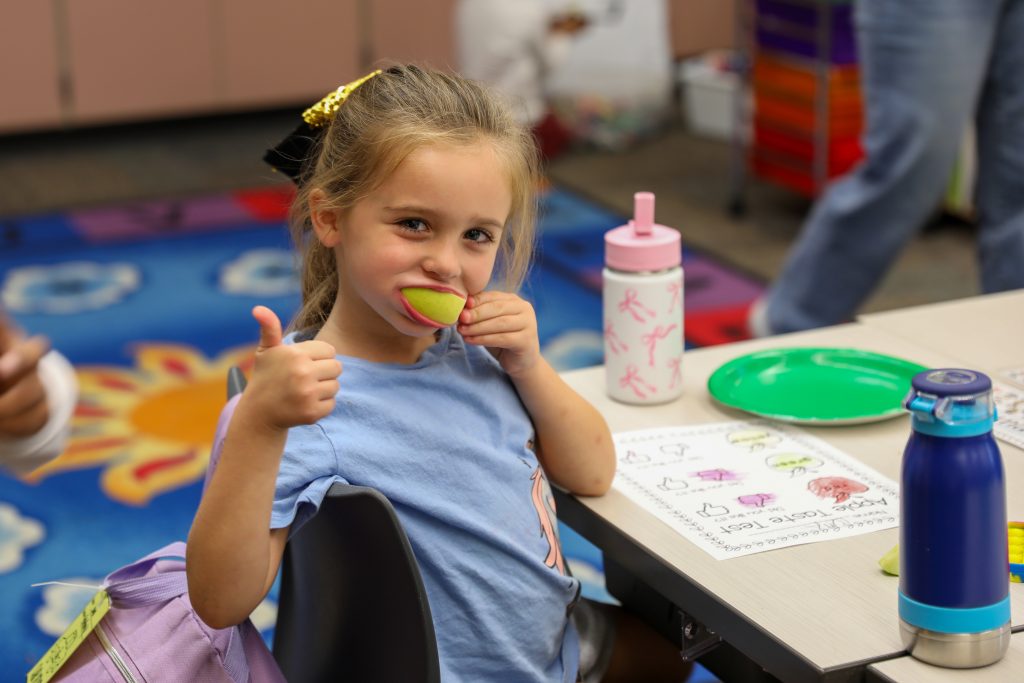 Kindergartener gives thumbs up while trying an apple slice.