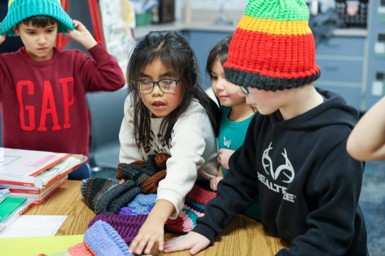 Kids playing with colorful knitted items at a table.
