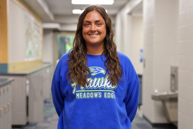 Woman in blue sweatshirt standing in hallway.