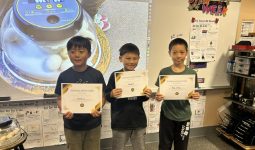 Three young boys proudly holding certificates in front of a classroom display.