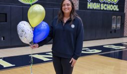 Woman in sports jersey holding balloons, smiling at camera, standing on basketball court.