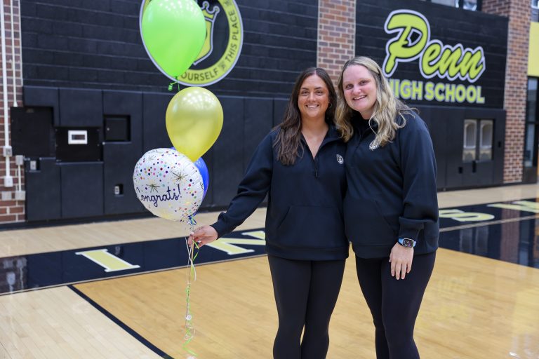 Two women posing in front of a basketball court with a sign that reads "Pine View High School".