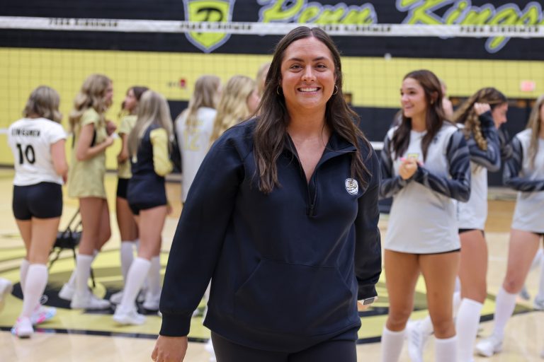 Woman in navy blue jacket standing in front of cheerleaders on court.