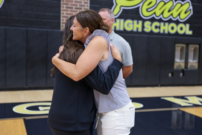 Two women posing in front of a basketball court. The woman on the left is wearing a black shirt and has short hair, while